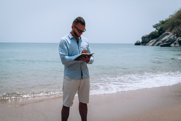 a young businessman in sunglasses, blue shirt and shorts writes in a notebook