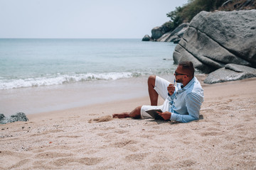 a young businessman in sunglasses, blue shirt and shorts writes in a notebook