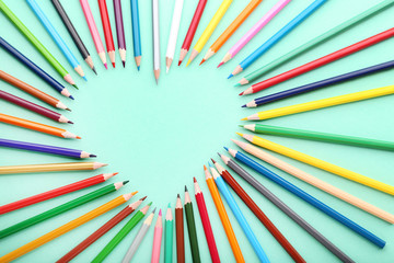 Colored pencils in heart shape on mint background