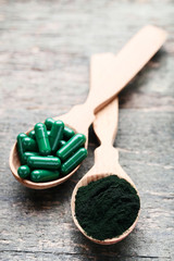 Spirulina powder and capsules in spoons on wooden table