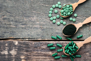 Spirulina powder and tablets in spoons on grey wooden table