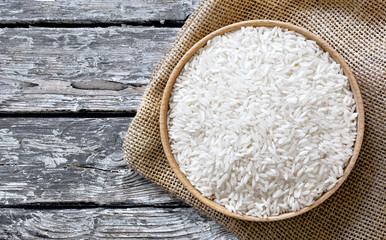 Healthy eating scene with raw parboiled rice in a wooden bowl, top view or closeup shot on a weathered wooden table.