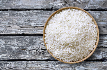 Healthy eating scene with raw parboiled rice in a wooden bowl, top view or closeup shot on a weathered wooden table.