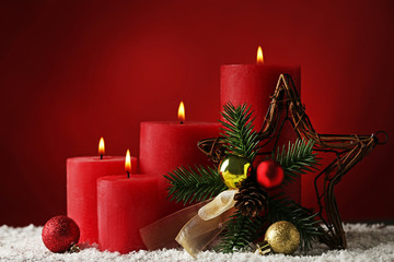 Christmas candle with fir-tree branches and baubles on red background