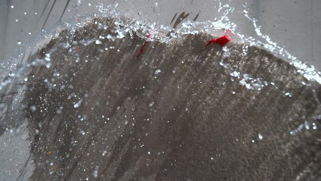 SLOW MOTION, CLOSE UP: Colorful water bomb exploding upon impact with the concrete panel. Cool shot of balloon filled with transparent liquid being thrown at the wall and bursting on a sunny day.
