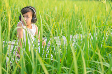 cute girl relaxing sitting and listening to music on the wooden bridge in the rice field on sun set with nature background. on the wooden bridge in the rice field on sun set with nature background.