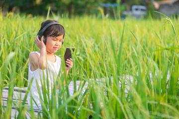 Asian cute girl relaxing sitting and using mobile phone on the wooden bridge in the rice field on sun set with nature background.