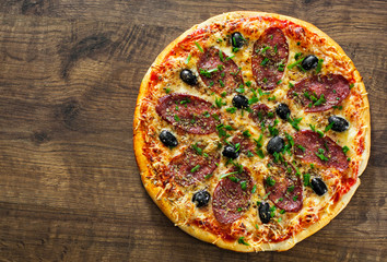 Pizza with Mozzarella cheese, salami, pepper, pepperoni, olives, Spices and Fresh Basil. Italian pizza on wooden background