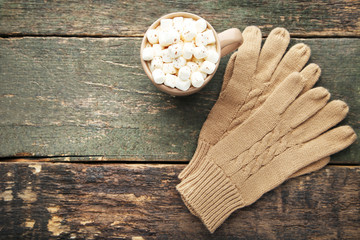 Knitted beige gloves and cup of coffee with marshmallow on wooden table