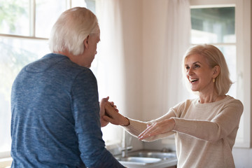 Old happy couple dancing in kitchen, mature family celebrating anniversary having fun together at home, middle aged caring husband holding hands of excited wife enjoying love, senior people lifestyle