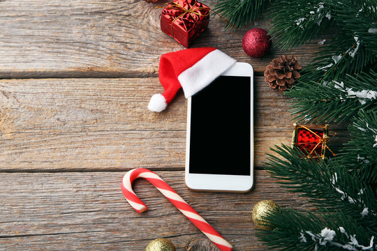 Smartphone with red santa hat and fir-tree branch on grey wooden table