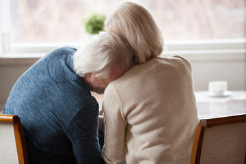 Rear back view at senior retired grey haired man leaning on shoulder of mature loving woman crying...
