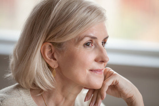 Dreamy thoughtful mature attractive woman relaxing hoping thinking of happy future, smiling senior middle aged lady looking away realizing positive thoughts feeling optimistic in good expectation