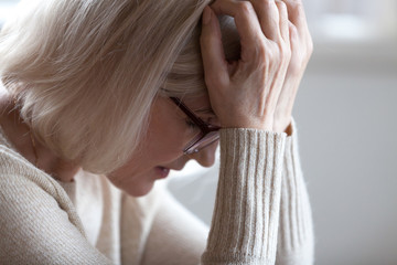 Stressed sad tired middle aged senior woman holding head in hands feeling headache migraine...