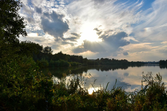 Beautiful landscape image of evening sun, behind clouds,  over Whitlingham Lake in Norfolk.