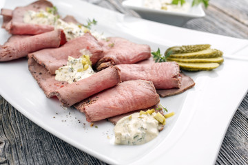 Traditional lunch meat with sliced cold cuts roast beef and remoulade as closeup on a white plate