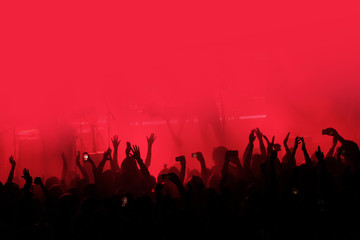 Red background with a crowd of cheering people at a concert. People with their hands up