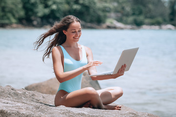 beautiful and sexy young woman sitting in lotus pose and medetiruet on a lounger with a laptop by the sea. woman freelancer doing yoga with a laptop in the beach resort