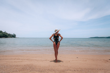 Summer lifestyle portrait of pretty young suntanned woman. Enjoying life  on the beach of the tropical island. Wearing stylish bikini and wide brimmed hat with stripes. Looking at the sea