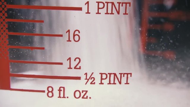 Slow motion pour white sugar into a glass measuring cup focus on numbers close up