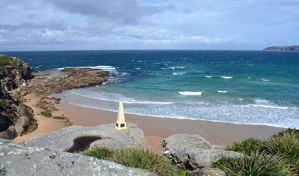 View of North Curl Curl beach on a sunny day. Cobbers Way obelisk in the foreground, rock pool and Tasman sea in the background.