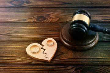 Judge's gavel, a broken heart of wood, a pair of gold wedding rings against a wooden table. Family law, divorce and conflict.