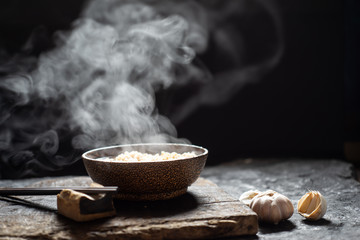 Noodles with steam and smoke in bowl on wooden background, selective focus. Asian meal on a table,...