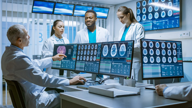 Team of Professional Medical Scientists Work in the Brain Research Laboratory. Neurologists / Neuroscientists Having Heated Discussion Surrounded by Monitors Showing CT, MRI Scans.