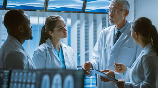 Meeting of the Team of Scientists in the Brain Research Laboratory. Neurologists / Neuroscientists Having Medical Discussion Surrounded by Monitors Showing CT, MRI Scans.