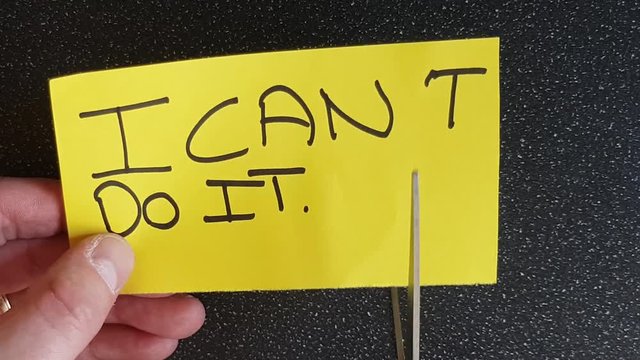 Man using scissors to remove the t from the word can't t leaving the positive motivational part. I can do it.