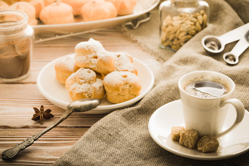 Cup of hot black coffee with home made profiteroles on a rustic wooden table.