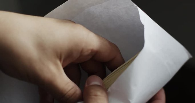 Closeup shot of man looks into the envelope which is pack of 100 dollar bills