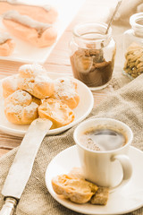 Home cooked profiteroles and eclairs with a cup of black coffee on a wooden table.