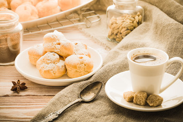 Cup of hot black coffee with home made profiteroles on a rustic wooden table.