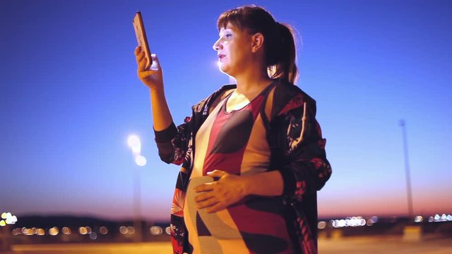 Estilo de vida y tecnologia.Mujer joven embarazada con su tel&eacute;fono inteligente en la calle de la ciudad.