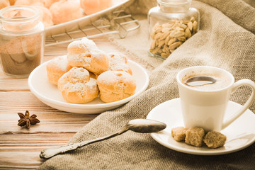 Cup of hot black coffee with home made profiteroles on a rustic wooden table.