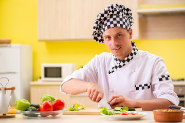 Young professional cook preparing salad at kitchen