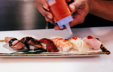 Chef squeezed hot sauce onto many kind of Japanese Sushi on ceramic plate