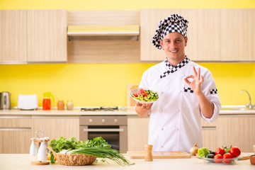 Young professional cook preparing salad at kitchen