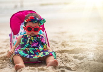 Adorable Baby Girl Wearing Sunglasses and Headband Sitting On A Carribean Beach