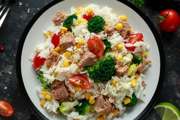 Fresh Tuna rice salad with sweet corn, cherry tomatoes, broccoli, parsley and lime in black bowl
