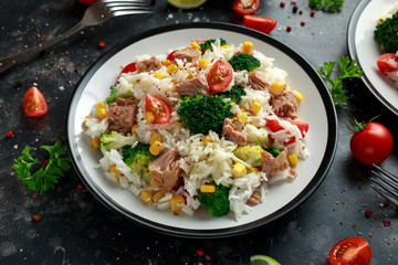 Fresh Tuna rice salad with sweet corn, cherry tomatoes, broccoli, parsley and lime in black bowl