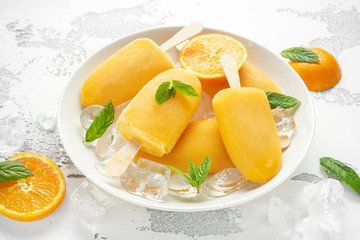 Popsicles, ice lollies on stick with sweet orange juice in white plate with ice