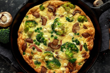 Homemade Frittata with mushrooms, broccoli, feta cheese, green peas and bacon on cast iron skillet