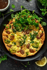 Homemade Frittata with mushrooms, broccoli, feta cheese, green peas and bacon on black plate