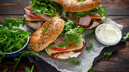 Fresh Bagels Sandwiches with cream cheese, bacon, tomato and green wild rocket on rustic wooden table