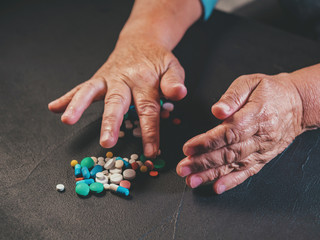 Grandmother counts multicolored tablets on black table at home. The concept of old age, medication,...