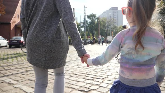Mother hold the hand of little kid daughter during walking down the street