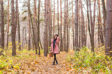 Fototapeta premium Autumn, nature and people concept - Portrait of beautiful smiling woman with brown suitcase walking in fall