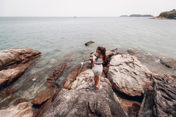 Young woman in white clothes looking at the sea, standing on the rocks